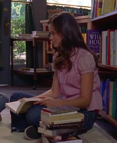 a woman sitting on the floor reading a book in front of a bookshelf