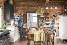 a man and woman standing in a kitchen next to a table