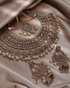 an elaborate necklace and earring set on a satin fabric with pearls, beads and other jewelry