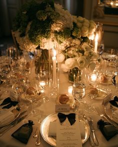 the table is set with silverware and white flowers in vases, candles, and menu cards