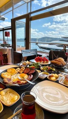 a table filled with plates and bowls of food next to large windows overlooking the water