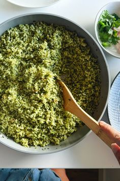 someone is holding a wooden spoon in a bowl full of green rice and other dishes