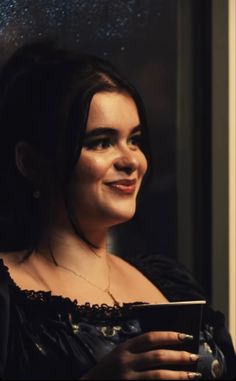 a woman in black dress looking out the window with rain falling down on her face