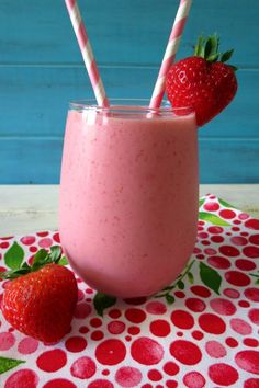 two strawberries sit on top of a pink smoothie