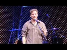 a man holding a microphone while standing in front of a chain link fence on stage