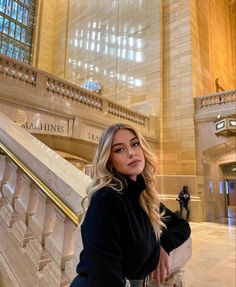 a woman is sitting on the stairs in a large building and posing for a photo