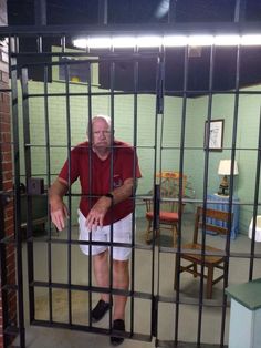 an older man standing behind bars in a jail cell