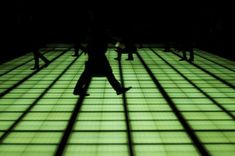 a group of people walking across a tiled floor in the dark with their shadows on them