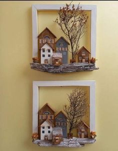 two frames with houses and trees on them are hanging on the wall in front of a yellow wall