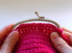 a hand holding a small purse with red yarn on the outside and pink crochet inside