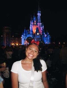 a woman standing in front of a castle with a minnie mouse ears on her head