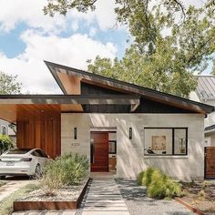 a white car is parked in front of a modern house with wood and stone accents