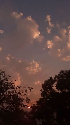 the sun is setting behind some trees and clouds in the sky, with only one cloud visible