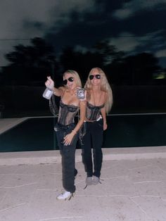 two women standing next to each other in front of a pool