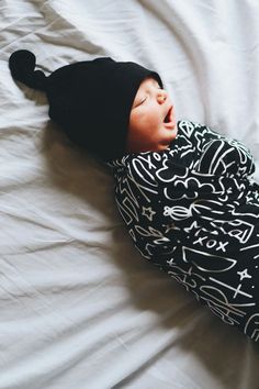 a baby wearing a black hat laying on top of a bed