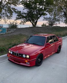 the red car is parked on the side of the road next to the water and trees