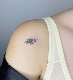 a small turtle tattoo on the back of a woman's left shoulder, which is attached to a bra