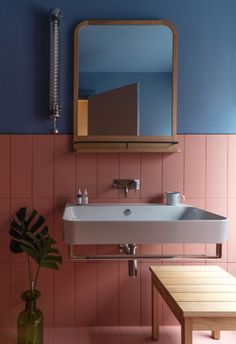 a sink and mirror in a room with pink tiles on the walls, wooden table and bench