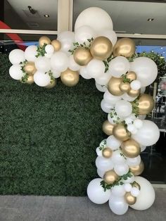 white and gold balloon arch with greenery on the top, in front of a green wall