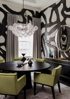 a dining room with black and white wallpaper, green chairs and a round table