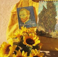 sunflowers are sitting next to a painting and a bag