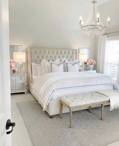 a large white bed sitting in a bedroom next to a window with a chandelier