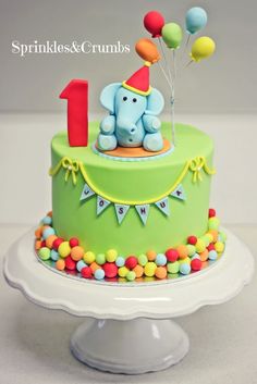 a green birthday cake with an elephant on top and balloons in the shape of 1