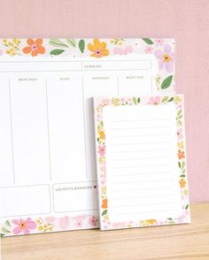 a desk with a notepad and pen on it next to a flowered wall