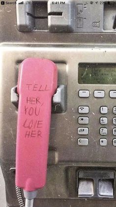 an old pay phone with writing on it and a pink cord attached to the telephone