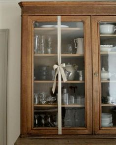 a wooden china cabinet with glass doors and bow on the top shelf, filled with dishes