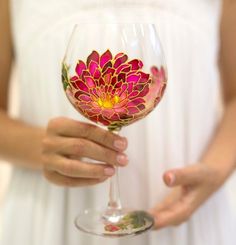 a woman holding a wine glass with a flower painted on it