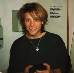 a man with long hair is smiling and holding a black object in his right hand