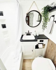 a white bathroom with black counter tops and wooden flooring, along with a round mirror above the sink