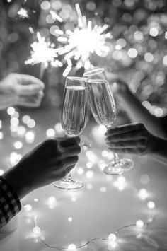 two people toasting with champagne glasses in front of fireworks and confetti on the table