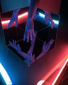 two hands reaching for each other in front of a mirror with neon lights on it