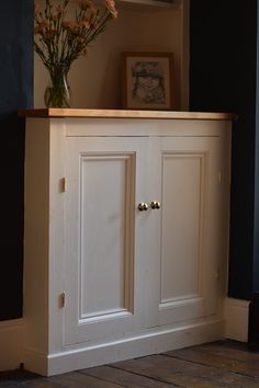 a white cabinet with two doors and some flowers on the top shelf next to it