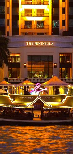 a boat is docked in front of a hotel at night with lights reflecting off the water