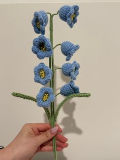 a crocheted blue flower is being held by a person's hand,