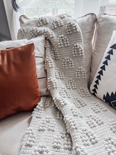 a white crocheted blanket sitting on top of a couch next to two pillows