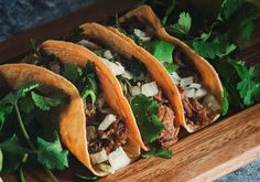 three tacos on a cutting board with limes and cilantro