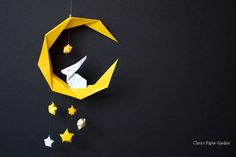 a yellow origami mobile with stars hanging from it's sides on a black wall