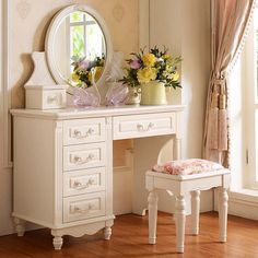 a white dressing table with flowers on it and a mirror in the corner next to it