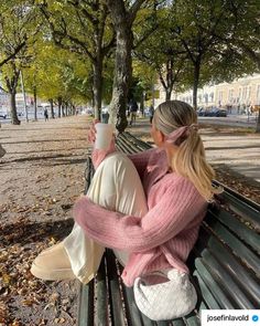 two women sitting on a park bench drinking coffee and looking at each other's hands