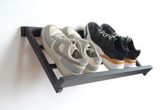 three pairs of shoes are sitting on a black shelf against a white wall and one pair is in the air