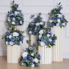 three white vases with blue and white flowers in them on a wooden floor next to a wall