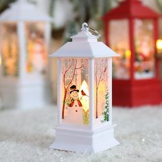 two small white lanterns with snowmen and trees in them on a carpeted floor