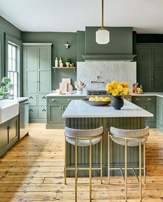 a large kitchen with green cabinets and white counter tops, yellow flowers on the island