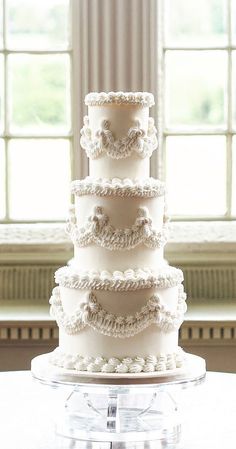 a three tiered white cake sitting on top of a glass stand in front of a window