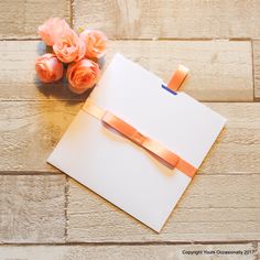 an open notepad with orange ribbon and flowers on wooden table next to brick wall