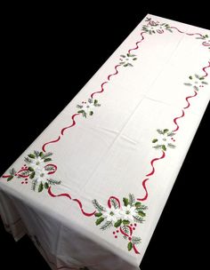 a white table cloth with red and green designs on the edges is sitting in front of a black background